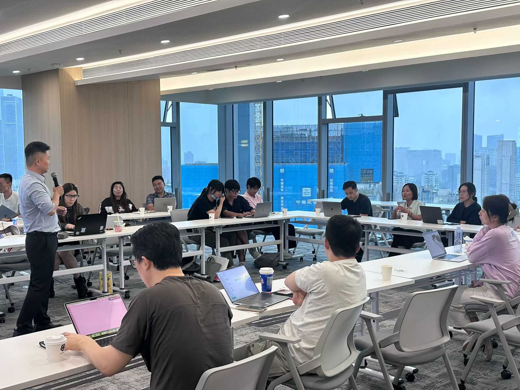 AI办公赋能千行百业系列 · 跨境电商工作坊现场,讲师持话筒讲解,参会者在长桌前使用电脑记录