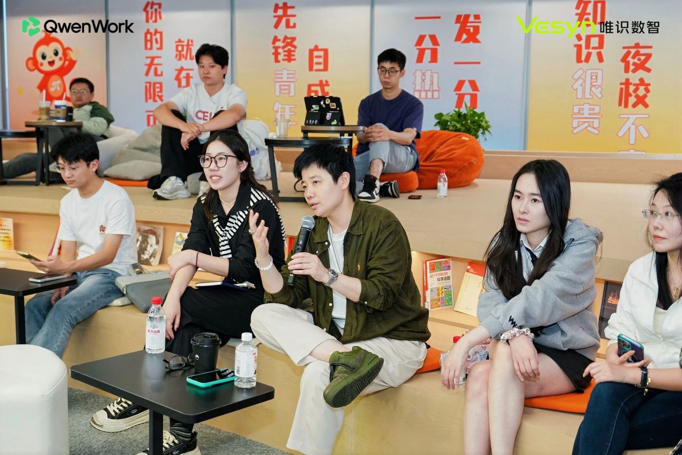参会者围坐在阶梯座位上参与交流,主持人持话筒发言